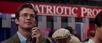Movie still from “Shattered Glass” (2003), directed by Billy Ray – A man with glasses is sitting in front of a patriotic sign; Close Up shot, Low angle