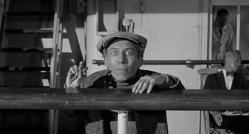 Movie still from “Ship of Fools” (1965), directed by Stanley Kramer – An older man holding a pipe while sitting at a table; Medium shot, High angle