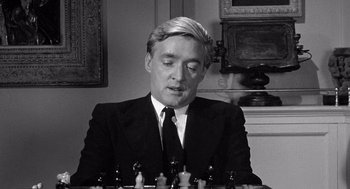 Movie still from “Ship of Fools” (1965), directed by Stanley Kramer – A black and white photo of a man in a suit playing chess; Close Up shot, Over the shoulder angle