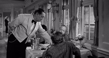Movie still from “Ship of Fools” (1965), directed by Stanley Kramer – A man serving a woman at a dinner table; Medium shot, Over the shoulder angle