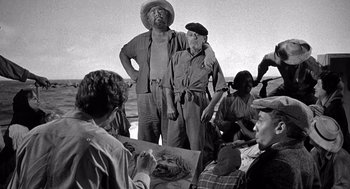 Movie still from “Ship of Fools” (1965), directed by Stanley Kramer – A group of men standing next to each other on a beach; Medium shot, Low angle