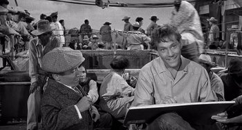Movie still from “Ship of Fools” (1965), directed by Stanley Kramer – A black and white photo of a man sitting on a boat; Medium shot, High angle