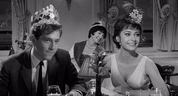 Movie still from “Ship of Fools” (1965), directed by Stanley Kramer – A man and a woman sitting at a table with a woman wearing a tiara; Medium shot, Low angle