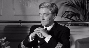 Movie still from “Ship of Fools” (1965), directed by Stanley Kramer – Black and white photograph of a man in a suit; Medium shot, Over the shoulder angle