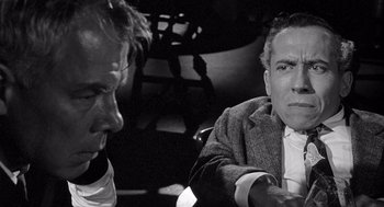 Movie still from “Ship of Fools” (1965), directed by Stanley Kramer – A man sitting next to another man on a chair; Close Up shot, Over the shoulder angle