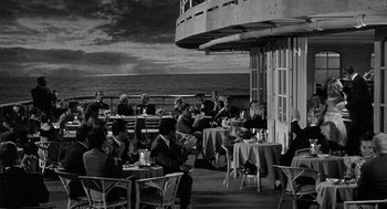 Movie still from “Ship of Fools” (1965), directed by Stanley Kramer – A group of people sitting at tables outside of a restaurant; Extreme Wide shot, High angle