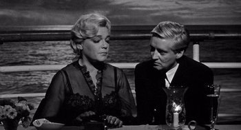 Movie still from “Ship of Fools” (1965), directed by Stanley Kramer – A woman and a man sitting at a dinner table; Medium shot, High angle