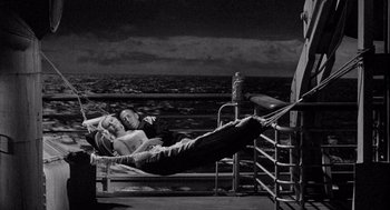 Movie still from “Ship of Fools” (1965), directed by Stanley Kramer – A man and a woman laying in a hammock on a pier; Wide shot, Overhead angle
