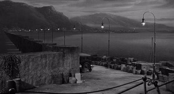 Movie still from “Ship of Fools” (1965), directed by Stanley Kramer – A black and white photo of a dock with a truck parked on the side of the road; Extreme Wide shot, High angle