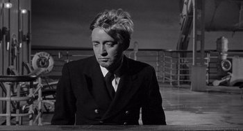 Movie still from “Ship of Fools” (1965), directed by Stanley Kramer – A black and white photo of a man in a suit and tie; Medium shot, Over the shoulder angle