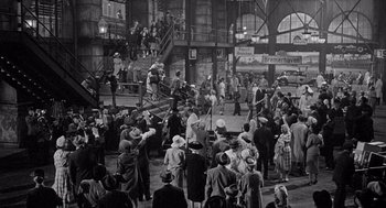Movie still from “Ship of Fools” (1965), directed by Stanley Kramer – A crowd of people standing in front of a train station; Extreme Wide shot, High angle