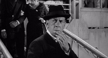 Movie still from “Ship of Fools” (1965), directed by Stanley Kramer – A man in a suit and a hat smoking a cigarette; Close Up shot, Over the shoulder angle