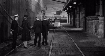 Movie still from “Ship of Fools” (1965), directed by Stanley Kramer – Three men and a woman are standing on a train track; Extreme Wide shot, High angle