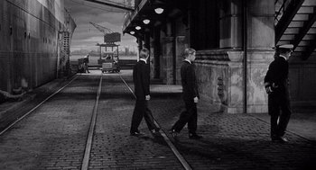 Movie still from “Ship of Fools” (1965), directed by Stanley Kramer – A couple of men walking down a street next to a building; Wide shot, High angle