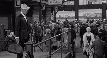Movie still from “Ship of Fools” (1965), directed by Stanley Kramer – A group of people standing in front of a train station; Wide shot, Over the shoulder angle