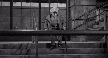 Movie still from “Ship of Fools” (1965), directed by Stanley Kramer – An older man in a hat and glasses is walking down some stairs; Wide shot, High angle