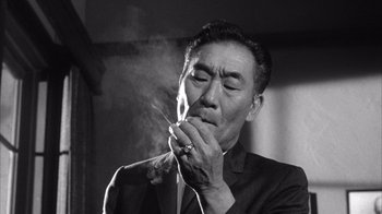 Movie still from “Shock Corridor” (1963), directed by Samuel Fuller – An older man smoking a cigarette in a suit; Close Up shot, Low angle