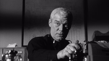 Movie still from “Shock Corridor” (1963), directed by Samuel Fuller – An older man holding a camera in front of a wall; Close Up shot, Low angle