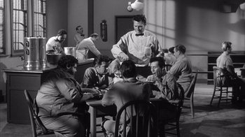 Movie still from “Shock Corridor” (1963), directed by Samuel Fuller – A group of people sitting around a table; Wide shot, High angle