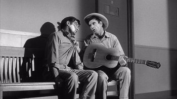 Movie still from “Shock Corridor” (1963), directed by Samuel Fuller – Two men sitting on a bench with a guitar; Medium shot, High angle
