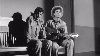 Movie still from “Shock Corridor” (1963), directed by Samuel Fuller – A man sitting next to another man while holding a guitar; Medium shot, Low angle