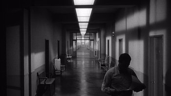 Movie still from “Shock Corridor” (1963), directed by Samuel Fuller – A man is walking down a hallway in a building; Wide shot, Low angle