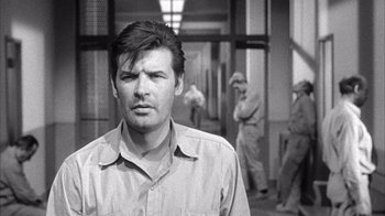 Movie still from “Shock Corridor” (1963), directed by Samuel Fuller – Black and white photograph of a man in front of other men; Close Up shot, Over the shoulder angle