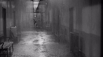 Movie still from “Shock Corridor” (1963), directed by Samuel Fuller – A person is walking in the rain in a building; Extreme Wide shot, High angle