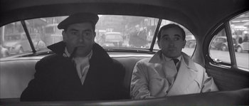 Movie still from “Shoot the Piano Player” (1960), directed by François Truffaut – A black and white photo of two men sitting in the back of a car; Medium shot, High angle