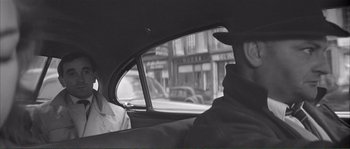 Movie still from “Shoot the Piano Player” (1960), directed by François Truffaut – A black and white photo of a man in the back of a car looking out the window; Medium shot, Over the shoulder angle