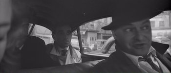 Movie still from “Shoot the Piano Player” (1960), directed by François Truffaut – A man in a suit sitting in the back of a car; Medium shot, Over the shoulder angle