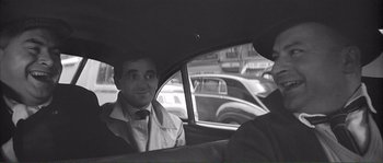 Movie still from “Shoot the Piano Player” (1960), directed by François Truffaut – A black and white photo of a man in the back of a car; Close Up shot, Over the shoulder angle