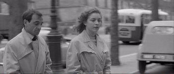 Movie still from “Shoot the Piano Player” (1960), directed by François Truffaut – A woman in a trench coat walking down a street; Medium shot, Over the shoulder angle
