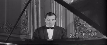 Movie still from “Shoot the Piano Player” (1960), directed by François Truffaut – A black and white photo of a man in a tuxedo playing a piano; Medium shot, High angle