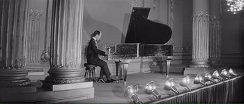 Movie still from “Shoot the Piano Player” (1960), directed by François Truffaut – A man sitting at a grand piano in a room; Wide shot, High angle