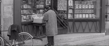 Movie still from “Shoot the Piano Player” (1960), directed by François Truffaut – A man standing on the side of the street looking at a box of records; Wide shot, Over the shoulder angle