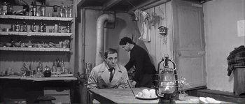 Movie still from “Shoot the Piano Player” (1960), directed by François Truffaut – A man sitting at a table in a room with another man standing next to him; Medium shot, High angle