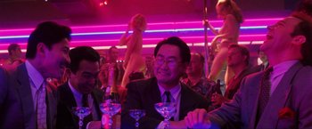 Movie still from “Showgirls” (1995), directed by Paul Verhoeven – A man sitting at a table in front of a group of people; Medium shot, Over the shoulder angle
