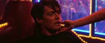 Movie still from “Showgirls” (1995), directed by Paul Verhoeven – A man with long dark hair is sitting in a dark room; Close Up shot, Over the shoulder angle
