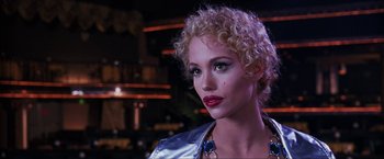 Movie still from “Showgirls” (1995), directed by Paul Verhoeven – A woman with blonde curly hair wearing a silver jacket; Close Up shot, Over the shoulder angle