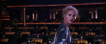 Movie still from “Showgirls” (1995), directed by Paul Verhoeven – A woman with blonde curly hair wearing a silver jacket; Medium shot, Over the shoulder angle