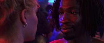 Movie still from “Showgirls” (1995), directed by Paul Verhoeven – A person with dreadlocks in a room; Close Up shot, Over the shoulder angle