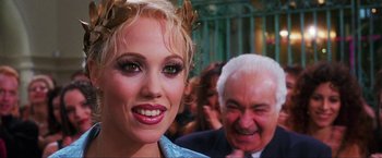 Movie still from “Showgirls” (1995), directed by Paul Verhoeven – A person smiling with a man in the background; Close Up shot, Over the shoulder angle