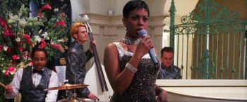 Movie still from “Showgirls” (1995), directed by Paul Verhoeven – A woman holding a microphone in front of a band; Medium shot, Low angle