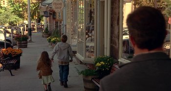 Movie still from “Signs” (2002), directed by M. Night Shyamalan – A woman and a child walking down the sidewalk; Wide shot, Over the shoulder angle
