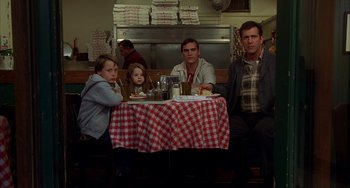 Movie still from “Signs” (2002), directed by M. Night Shyamalan – Four people sitting at a table in front of a checkered tablecloth; Wide shot, Over the shoulder angle