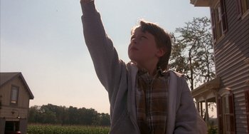 Movie still from “Signs” (2002), directed by M. Night Shyamalan – A young boy holding his hand up in the air; Medium shot, Low angle
