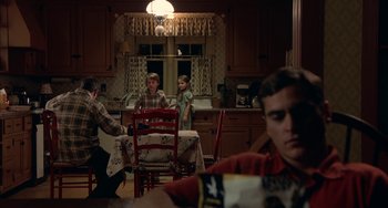 Movie still from “Signs” (2002), directed by M. Night Shyamalan – A group of people sitting around a table in a kitchen; Medium shot, Over the shoulder angle