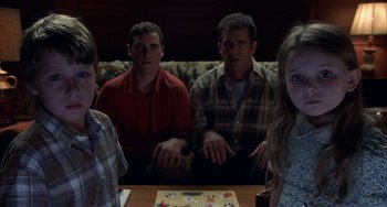 Movie still from “Signs” (2002), directed by M. Night Shyamalan – A group of people sitting around a wooden table; Medium shot, High angle