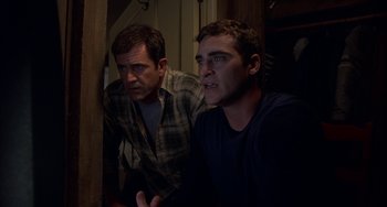 Movie still from “Signs” (2002), directed by M. Night Shyamalan – Two men are sitting next to each other in a room; Medium shot, Over the shoulder angle
